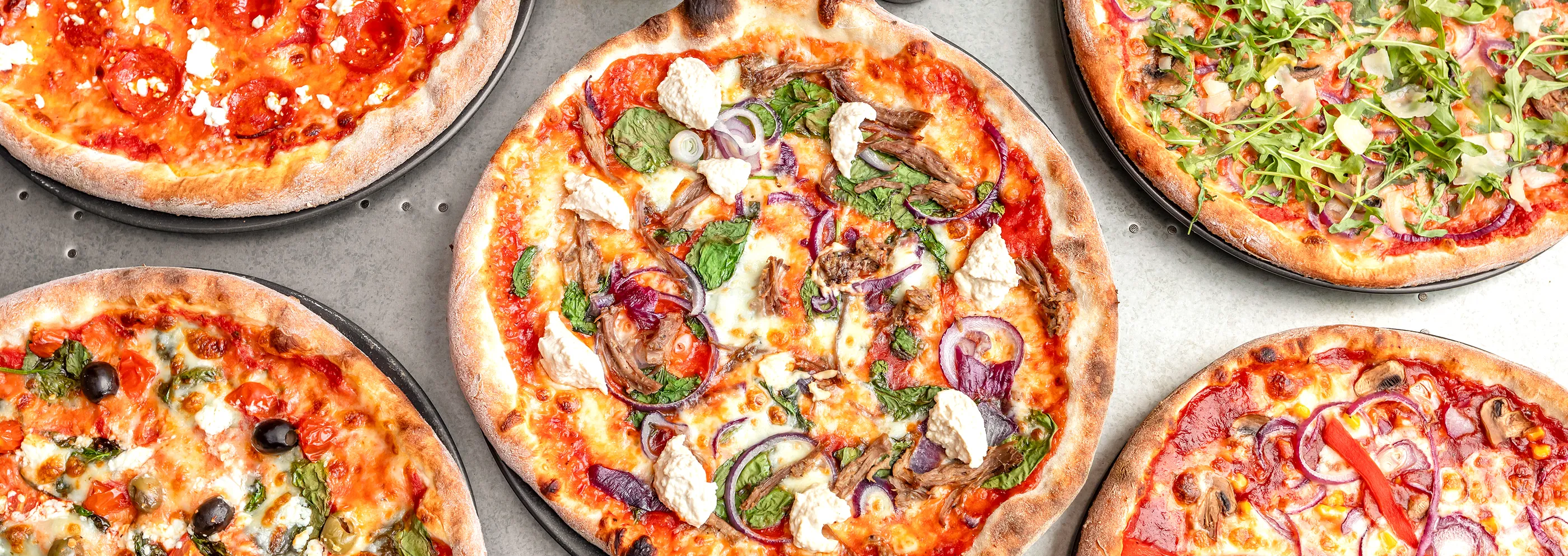 A table of freshly baked @homepizza pizzas: pepperoni and feta, rocket, slow-cooked lamb and roasted veg.
