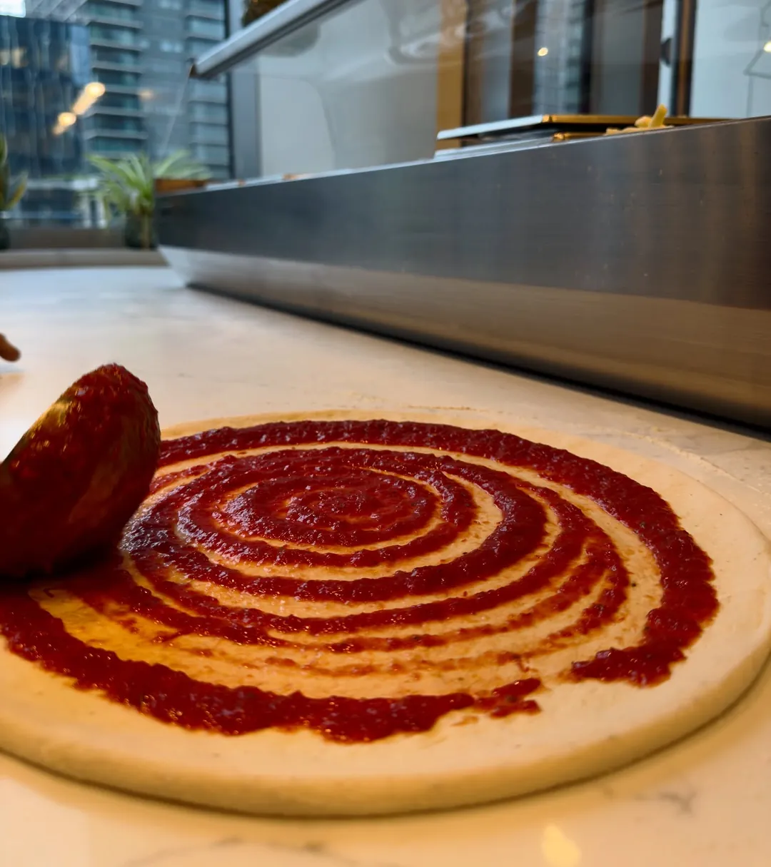 Tomato sauce being spiralled onto a hand-stretched base.