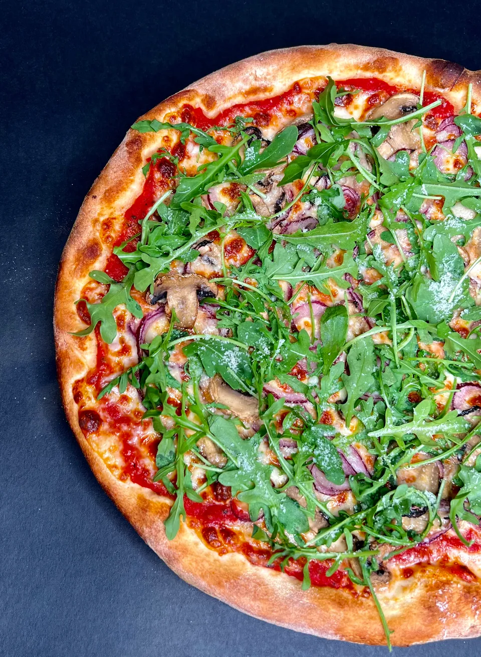 Rocket, mushroom and red onion pizza on a dark background.