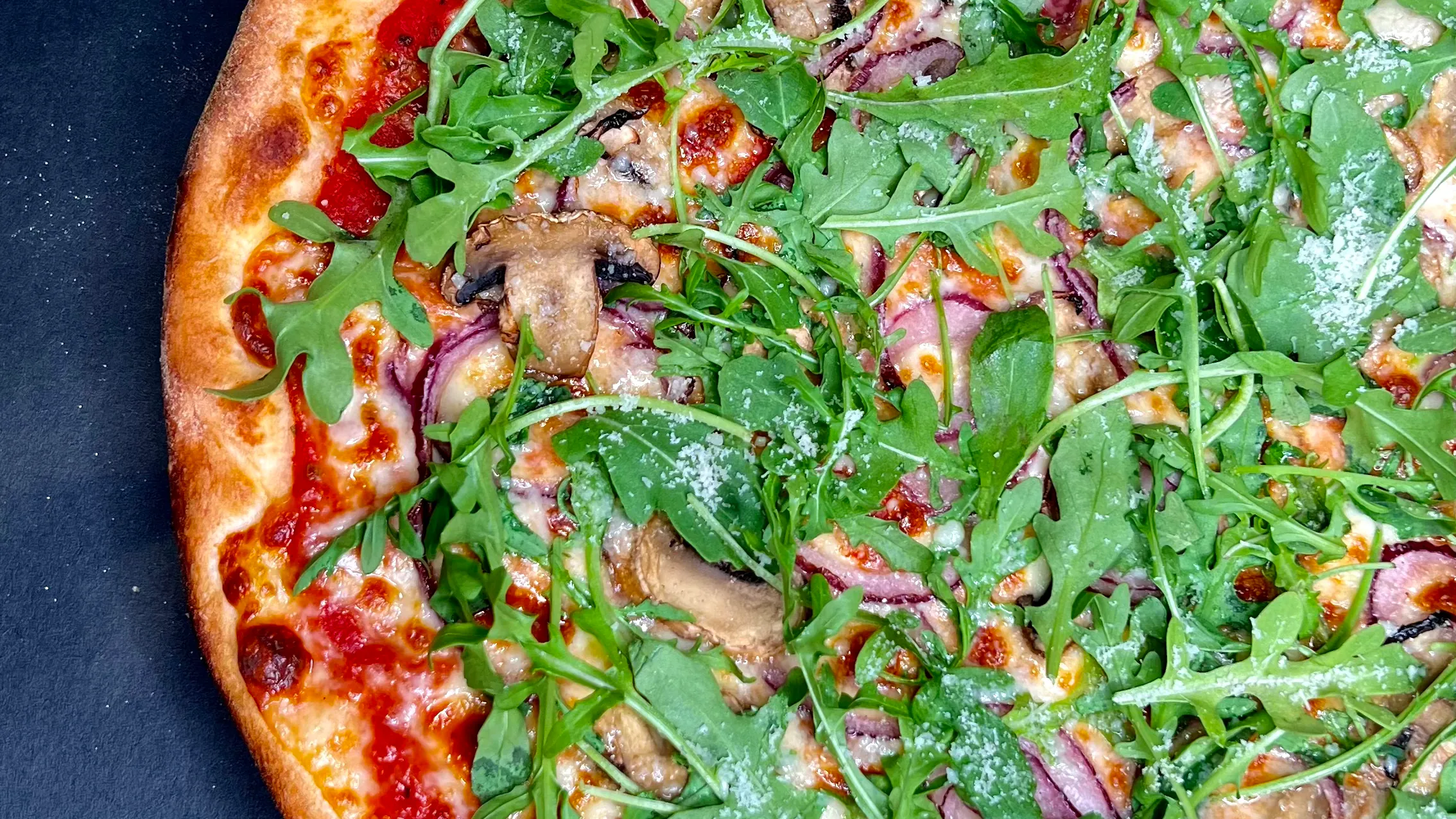 A rocket, mushroom and red onion pizza on a dark background.