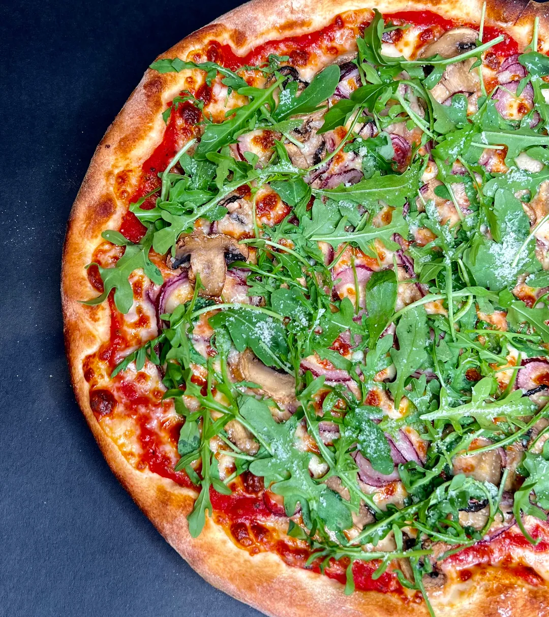 A rocket, mushroom and red onion pizza with a golden, blistered crust.